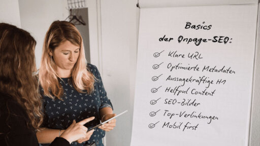 Zwei Mitarbeiterinnen neben einem Flipchart, auf dem die "Basics der Onpage-SEO" stehen, um das Fundament einer erfolgreichen Onpage Suchmaschinenoptimierung zu legen.