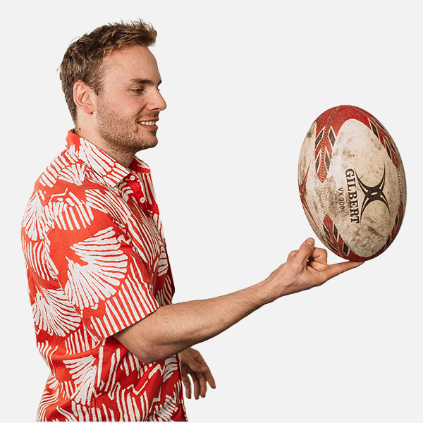 Florian Benhauser in einem roten Hawaii-Hemd, dreht einen Rugby-Ball auf seiner Hand, vor weißem Hintergrund.