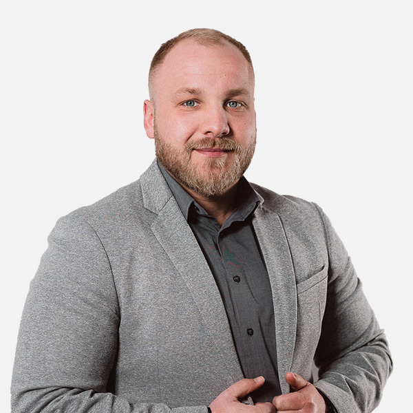 Florian Michel in einem grauen Blazer mit dunklem Hemd, lächelt selbstbewusst in die Kamera. Er hat einen kurzen Bart und einen modernen Haarschnitt. Weißer Hintergrund.