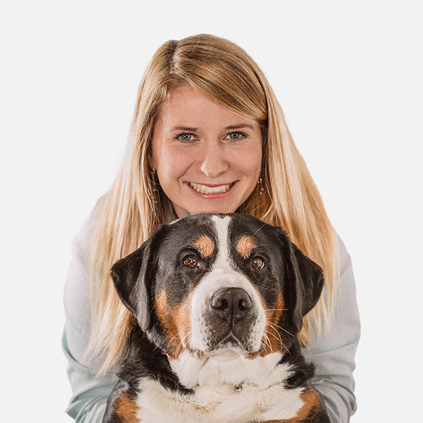 Jana Grube mit langen, blonden Haaren lächelt freundlich in die Kamera. Vor ihr sitzt ein großer, dreifarbiger Berner Sennenhund mit aufmerksamem Blick. Der Hintergrund ist weiß.