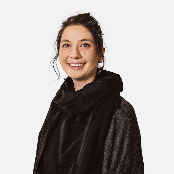 Jasmin Hoedt trägt einen schwarzen Schal und eine dunkle Jacke, während sie freundlich in die Kamera lächelt, vor einem weißen Hintergrund.