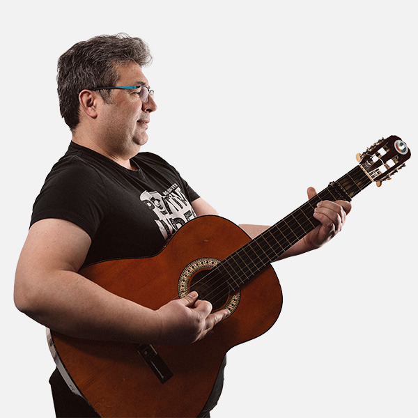 Kaya Küçük spielt auf einer klassischen Gitarre, trägt ein schwarzes T-Shirt mit Print und eine Brille, seitliche Ansicht vor weißem Hintergrund.