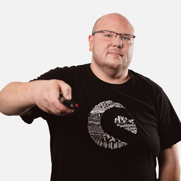 Marc Roba in schwarzem T-Shirt mit Shopware Design, hält eine Fernbedienung in der Hand, vor weißem Hintergrund.