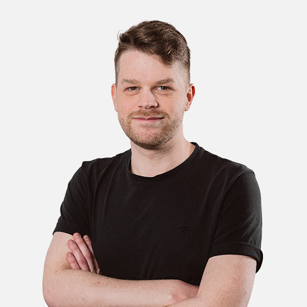 Maurice Schwarze mit verschränkten Armen, trägt ein schwarzes T-Shirt und blickt freundlich in die Kamera vor weißem Hintergrund.