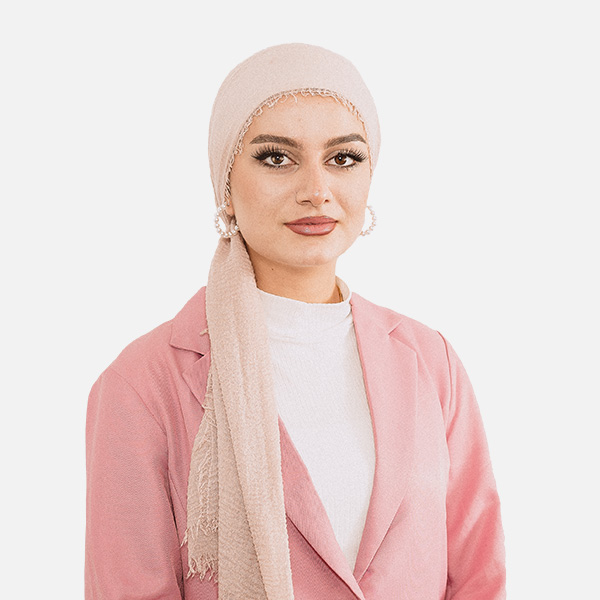 Porträt von Shahed Hamo mit beigem Kopftuch und rosa Blazer vor weißem Hintergrund.