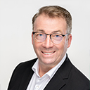 Porträt von Guido Wieling, Geschäftsführer von tproperty, mit freundlichem Lächeln und Brille vor neutralem Hintergrund.