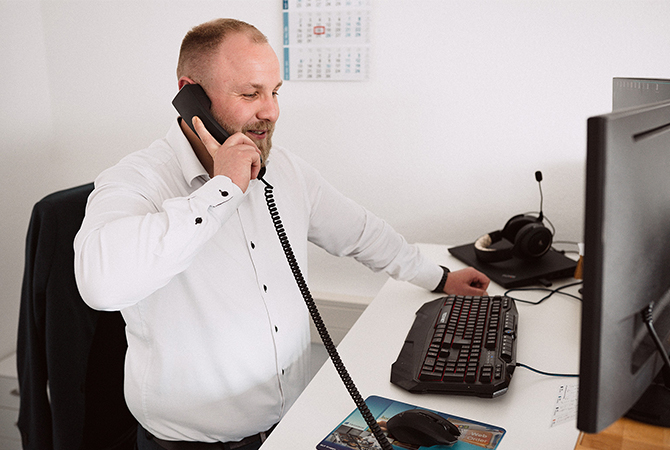 YTPI Vertriebsmitarbeiter berät einen Kunden am Telefon an seinem Schreibtisch mit Monitor, Tastatur und Headset.