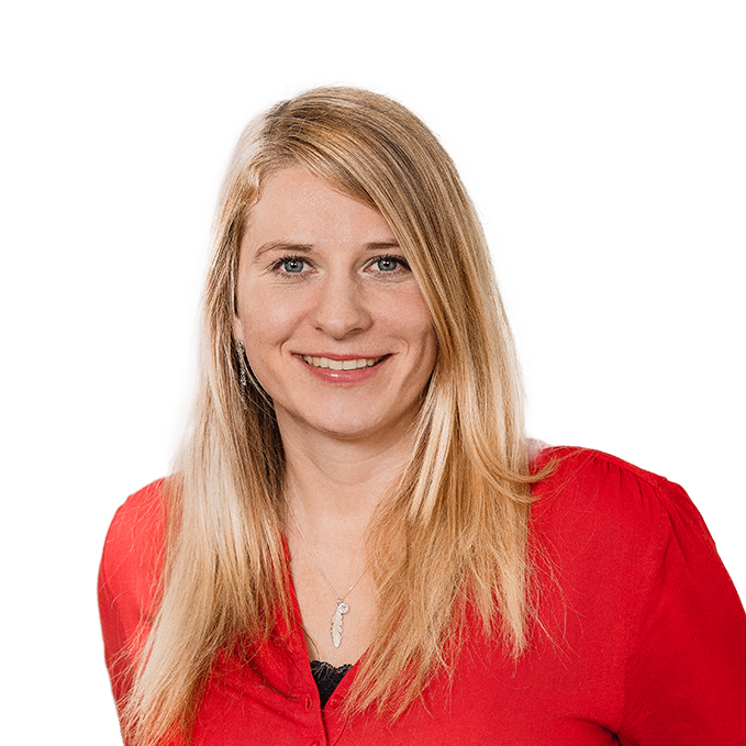 Jana Grube mit langen, blonden Haaren, lächelt freundlich in die Kamera. Sie trägt eine rote Bluse und eine silberne Kette mit Anhänger. Der Hintergrund ist weiß.