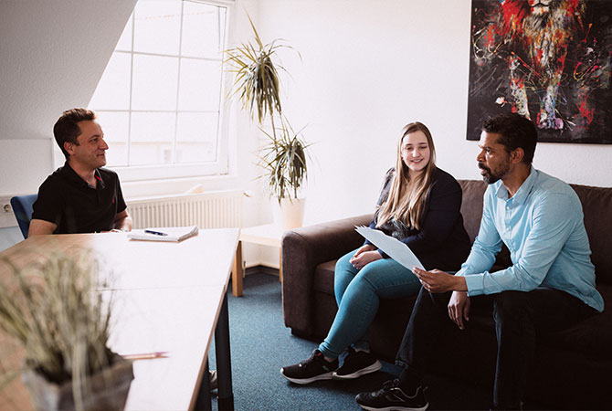 Drei Personen, alle sitzend, in lockerer Büroumgebung im Gespräch über die Betreuung einer Website.