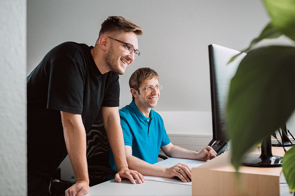 Zwei Männer aus dem Online-Marketing arbeiten gemeinsam an einem Arbeitsplatz mit Monitor.