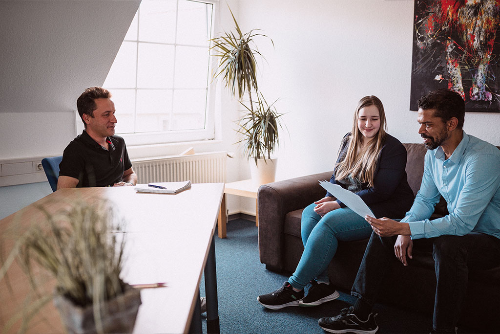 Drei Personen in Besprechung zum Online-Marketing, zwei auf dem Sofa, eine am Schreibtisch sitzend.