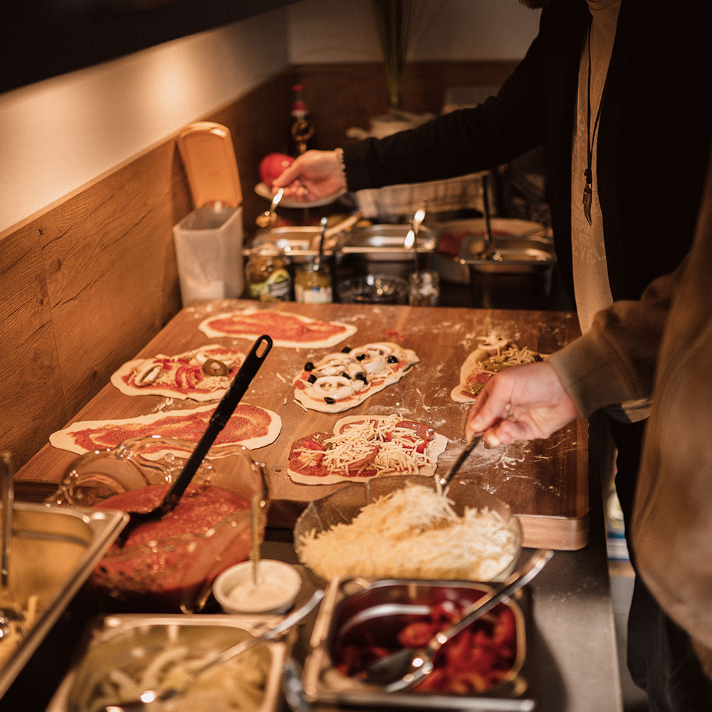 emeinsamer Pizzaabend im Team – Mitarbeitende belegen ihre Pizzen mit frischen Zutaten beim kreativen Teamevent in der Agenturküche