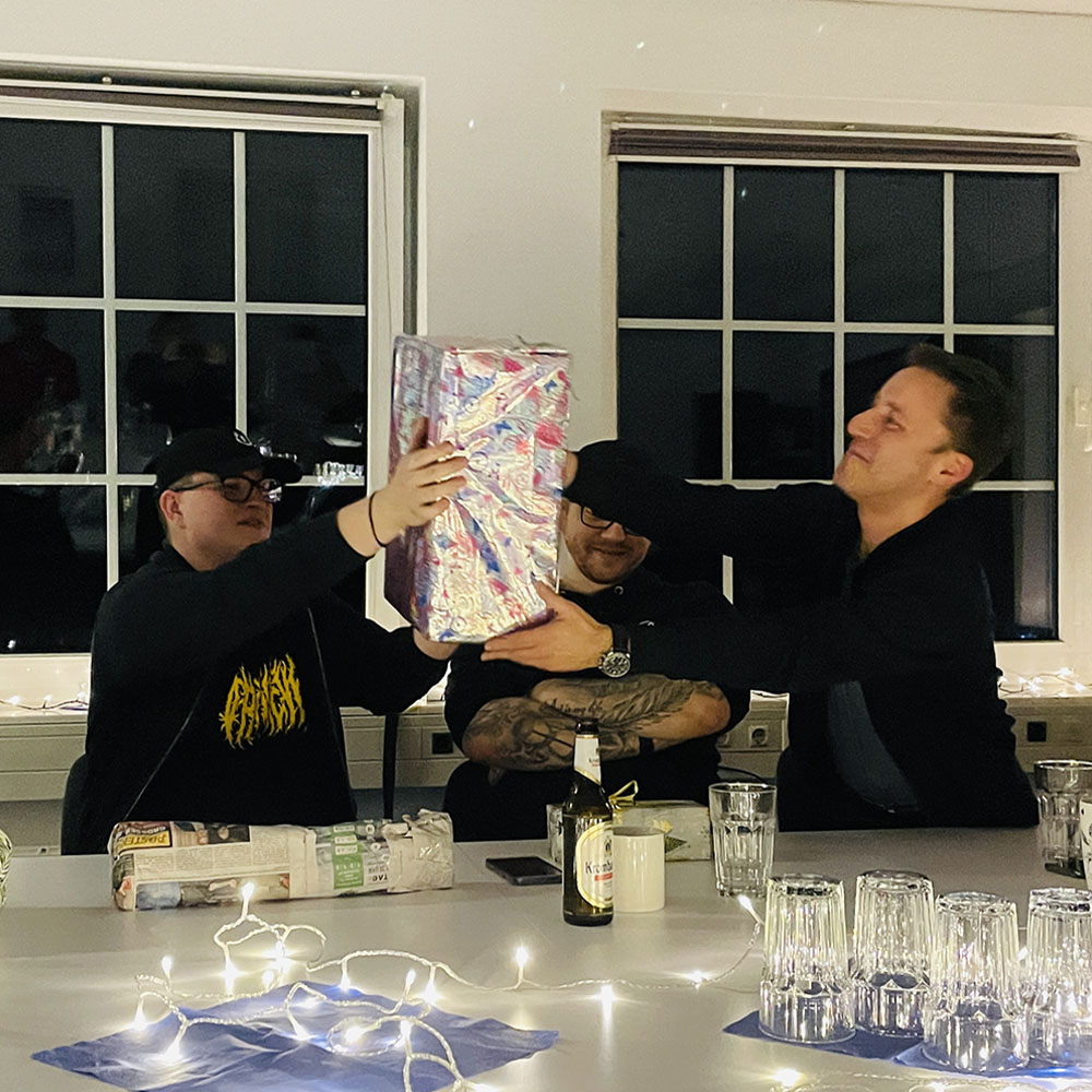 Teamevent mit Weihnachtswichteln in der Agentur – Mitarbeitende überreichen sich ein bunt verpacktes Geschenk mit viel Spaß und Gelächter