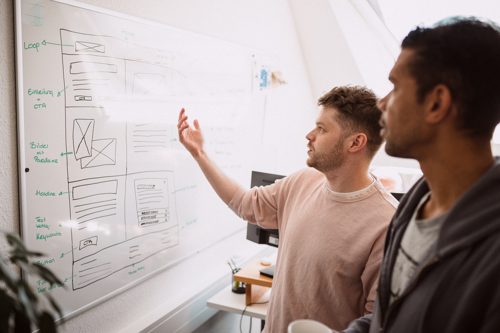 Zwei Mitarbeiter besprechen die Webseiten-Konzeption und UX-Strategie an einem Whiteboard