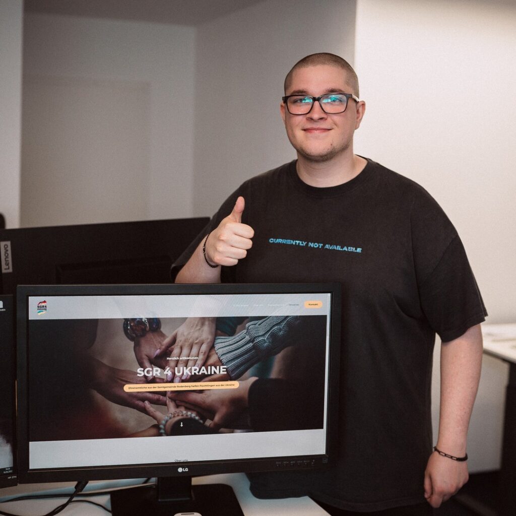 Webdesigner präsentiert stolz die fertige Website am Monitor – Projektabschluss mit Fokus auf Design, Umsetzung und sozialem Engagement
