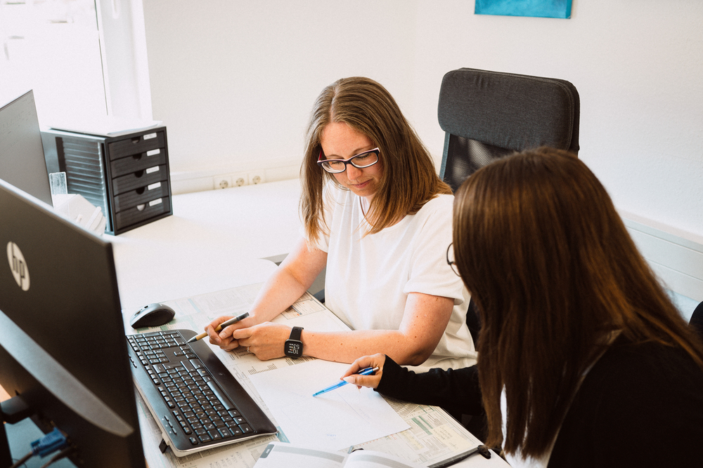 Zwei Mitarbeiterinnen der Agentur YTPI bei einer Beratung am Arbeitsplatz mit PC und Unterlagen.