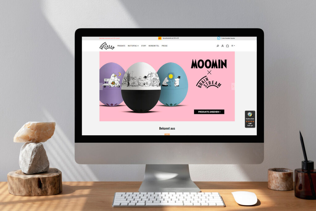 Desktop-Monitor auf Holzschreibtisch zeigt Produktübersicht eines Onlineshops auf basis von Shopware mit Filtermenü und Preisen.